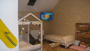A bedroom with a bunk bed, a small rocking chair, a TV mounted on the wall, and a wooden shelf with books.