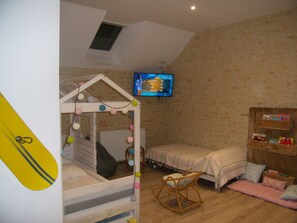 A bedroom with a bunk bed, a small rocking chair, a TV mounted on the wall, and a wooden shelf with books. - Mansion - Fourches (Fourches)