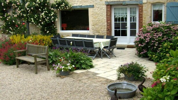 An outdoor patio with a table and chairs, surrounded by various plants and flowers.