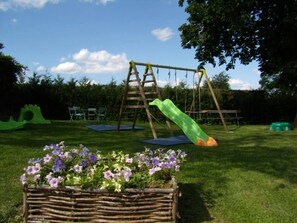 A wooden swing set with a green slide, a ladder, and a flower bed with purple flowers. - Mansion - Fourches (Fourches)