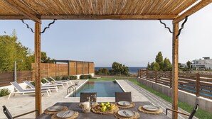 A covered outdoor dining area with a pool, lounge chairs, and a view of the sea. - Brand New Top Luxury Villa!  Stunning modern, extremely stylish. (Afandou)