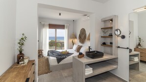 A modern bedroom with a large bed, a bathroom with a black sink, and a view of the sea. - Brand New Top Luxury Villa!  Stunning modern, extremely stylish. (Afandou)