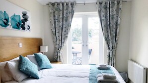 A hotel room with a bed, pillows, a bedside table, a lamp, a window with curtains, and a view of the outside. - 2 Bed / 2 Bath Contemporary apartment. Close to beach, Lift access & Parking 4*  (Bournemouth)