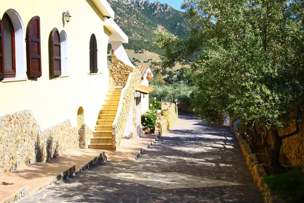 A stone pathway leading to a building with arched windows and a stone wall. - House / Villa - VILLASIMIUS SOLANAS (Solanas)