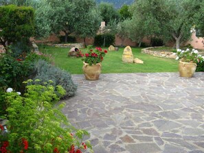 Un jardín con un patio de piedra, plantas variadas y una estatua.