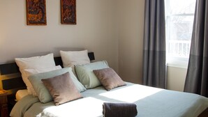 Une chambre avec un grand lit, un luminaire suspendu et deux œuvres d’art encadrées accrochées au mur.