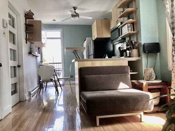 A modern kitchen with a microwave, stove, and wooden cabinets. There is a dining area with a chair and a small table.