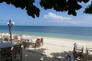 A beachside restaurant with wooden tables and chairs, overlooking a clear blue sea.