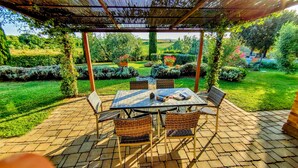 An outdoor patio with a table and chairs, surrounded by a garden with various plants and a view of the countryside.