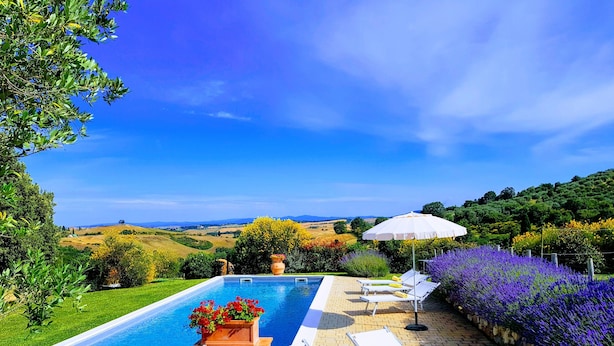 A pool area with lounge chairs and a table, surrounded by a garden with purple flowers and a view of rolling hills. - Montalcino: Private villa in the heart of Tuscany, private pool, A/C (Montisi)