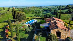 A villa with a swimming pool, stone architecture, and a view of rolling hills.