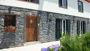 A stone facade with a wooden door, green shutters, and flower boxes. - Typical Madeiran House in Calheta, Madeira (Estreito da Calheta)