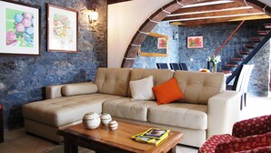 A living room with a stone wall, a wooden staircase, and a sofa with a cushion. - Typical Madeiran House in Calheta, Madeira (Estreito da Calheta)
