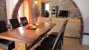 A dining area with a wooden table, chairs, and a flower centerpiece. There is a sofa and a television in the background. - Typical Madeiran House in Calheta, Madeira (Estreito da Calheta)