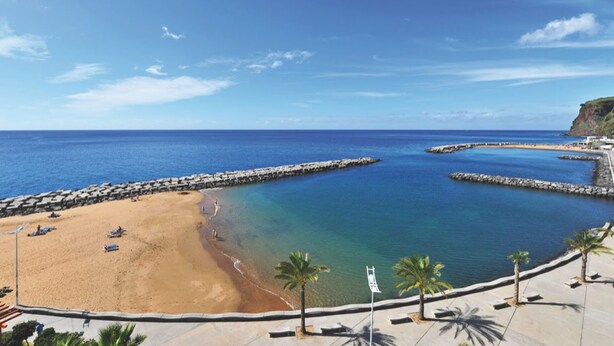 A beach with clear blue water, a sandy shore, and a rocky breakwater. - Typical Madeiran House in Calheta, Madeira (Estreito da Calheta)