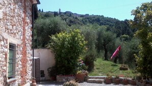 A stone building with a garden area, potted plants, and a view of a hill with a castle in the background. - Rustic first hill sea view in Versilia (Pietrasanta)