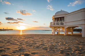 Een strand met een wit gebouw, voorzien van een balkon en een koepel.