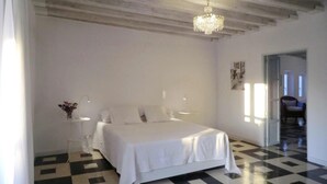 A bedroom with a checkered floor, a bed with white linens, a chandelier, and a door leading to another room. - 4th floor apartment in historic Cadiz, and just a 10 minutes walk to the beach. (CADIZ)