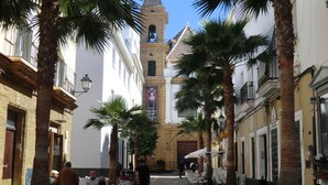A cobblestone street lined with palm trees and buildings, featuring outdoor seating areas and a prominent church tower in the background. - 4th floor apartment in historic Cadiz, and just a 10 minutes walk to the beach. (CADIZ)