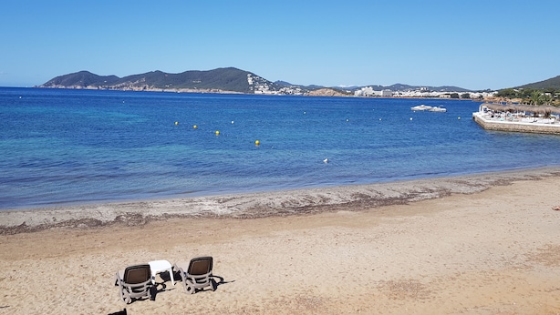 A beach with clear blue water, a sandy shore, and a few chairs. - House with pool 200 meters from the beach (S'Argamassa)