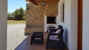 A covered outdoor seating area with stone walls, a fireplace, and wicker furniture. - House with pool 200 meters from the beach (S'Argamassa)