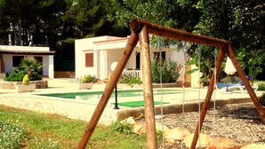 A wooden swing set in a garden area with a pool and a building in the background. - House with pool 200 meters from the beach (S'Argamassa)