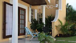 A covered porch with a wooden ceiling, a white door, and a blue and white striped chair.