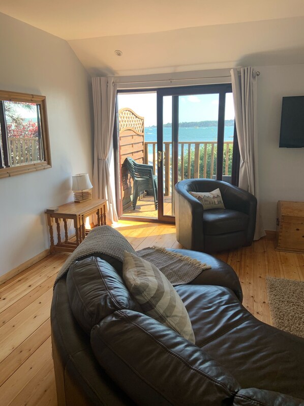A cozy living room with a leather sofa, a wooden coffee table, and a view of the sea through a sliding glass door.