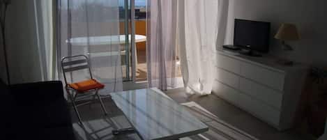 A modern living room with a glass table, a chair, a TV, and a lamp.