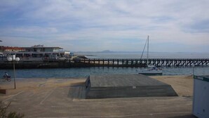 Vista costera con un muelle que se adentra en el agua, una lancha amarrada y un edificio con balcón que da al mar.