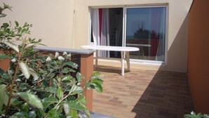 Un patio con una mesa y sillas, una puerta corrediza de vidrio y suelo de ladrillo.
