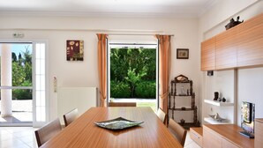 Een eetgedeelte met een houten tafel, stoelen en uitzicht op groen via een glazen deur.