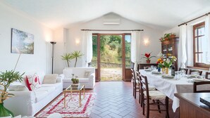 Een ruime woonkamer met een witte bank, een salontafel en een eettafel voor zes personen. Een groot raam biedt uitzicht op de tuin.