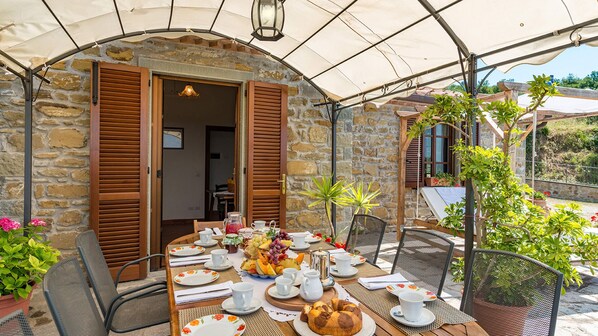An outdoor dining area with a stone wall backdrop, wooden shutters, and a covered patio. - Villa Fabi 6+2, Emma Villas (Cortona)
