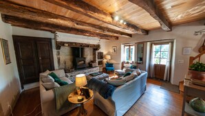 Una sala de estar acogedora con chimenea, vigas de madera, un sofá y una mesa con lámpara.