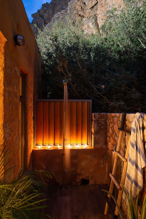 A stone-walled outdoor area with a wooden fence, a hanging light fixture, and a wooden ladder leaning against the wall.