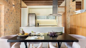 Un área de comedor con una mesa negra, sillas blancas, una pared de piedra, un armario de madera y una cocina al fondo.