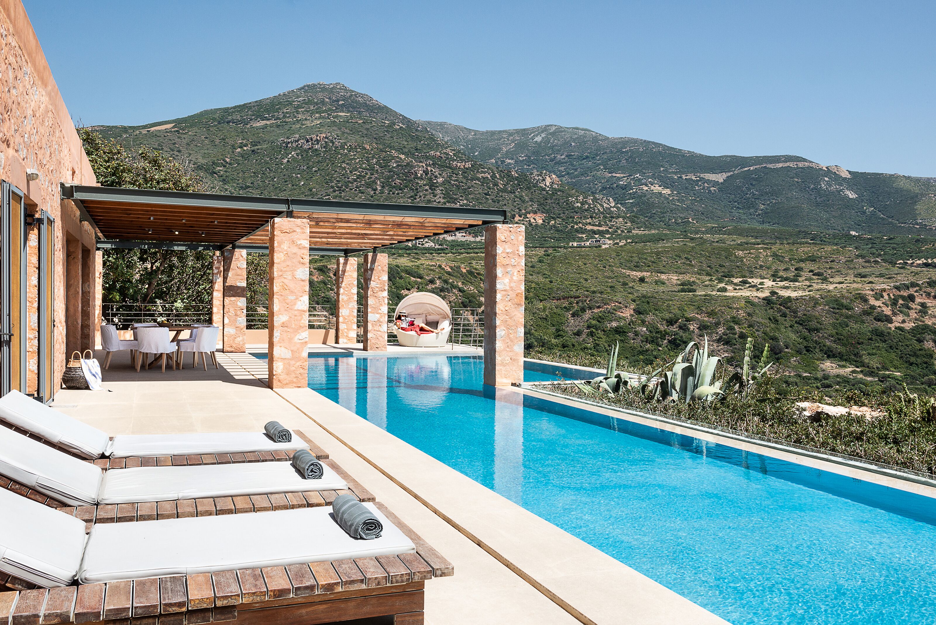 Zona de piscina con sillones de descanso, una pérgola y vistas a las montañas.