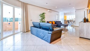 A spacious living area with a blue sofa, a dining table, and a kitchen area in the background. - Full private villa - 300sqm Hammam Jacuzzi Heated Pool Billiard BBQ - Ideal & quiet location (Albufeira)