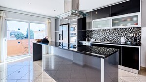 A modern kitchen with a central island, black and white tiled backsplash, and a view of the city through large windows. - Full private villa - 300sqm Hammam Jacuzzi Heated Pool Billiard BBQ - Ideal & quiet location (Albufeira)