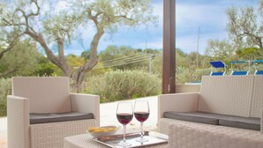 A patio area with wicker furniture, two glasses of red wine, and a tray with chips.