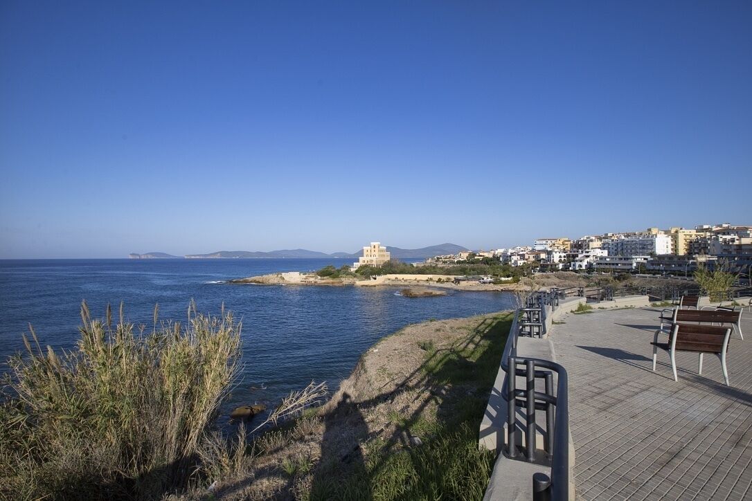 Une promenade en bord de mer offrant une vue sur la mer, un banc de parc et un bâtiment à la façade de couleur claire.