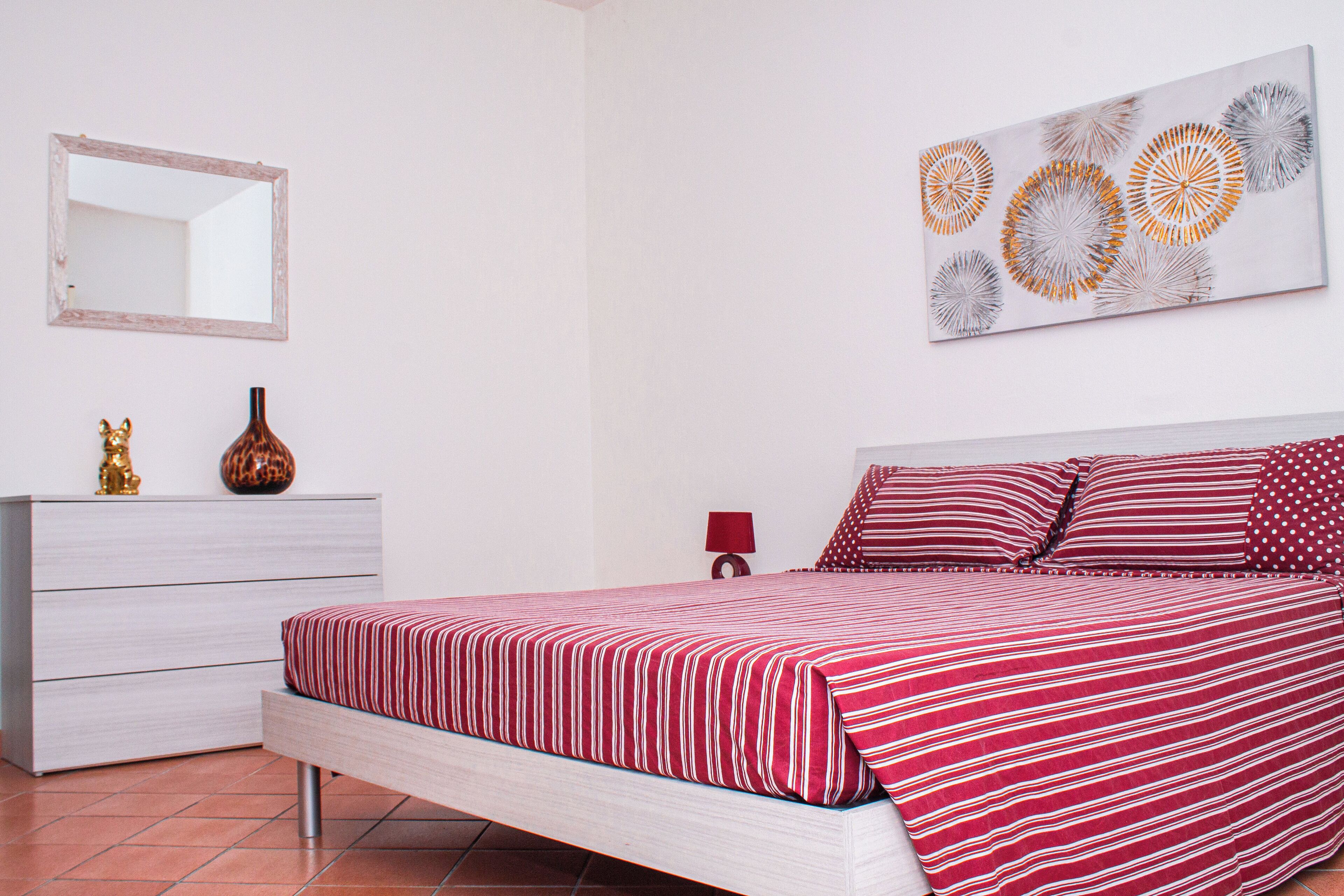 Un dormitorio con cama, cómoda, espejo y una obra de arte en la pared.