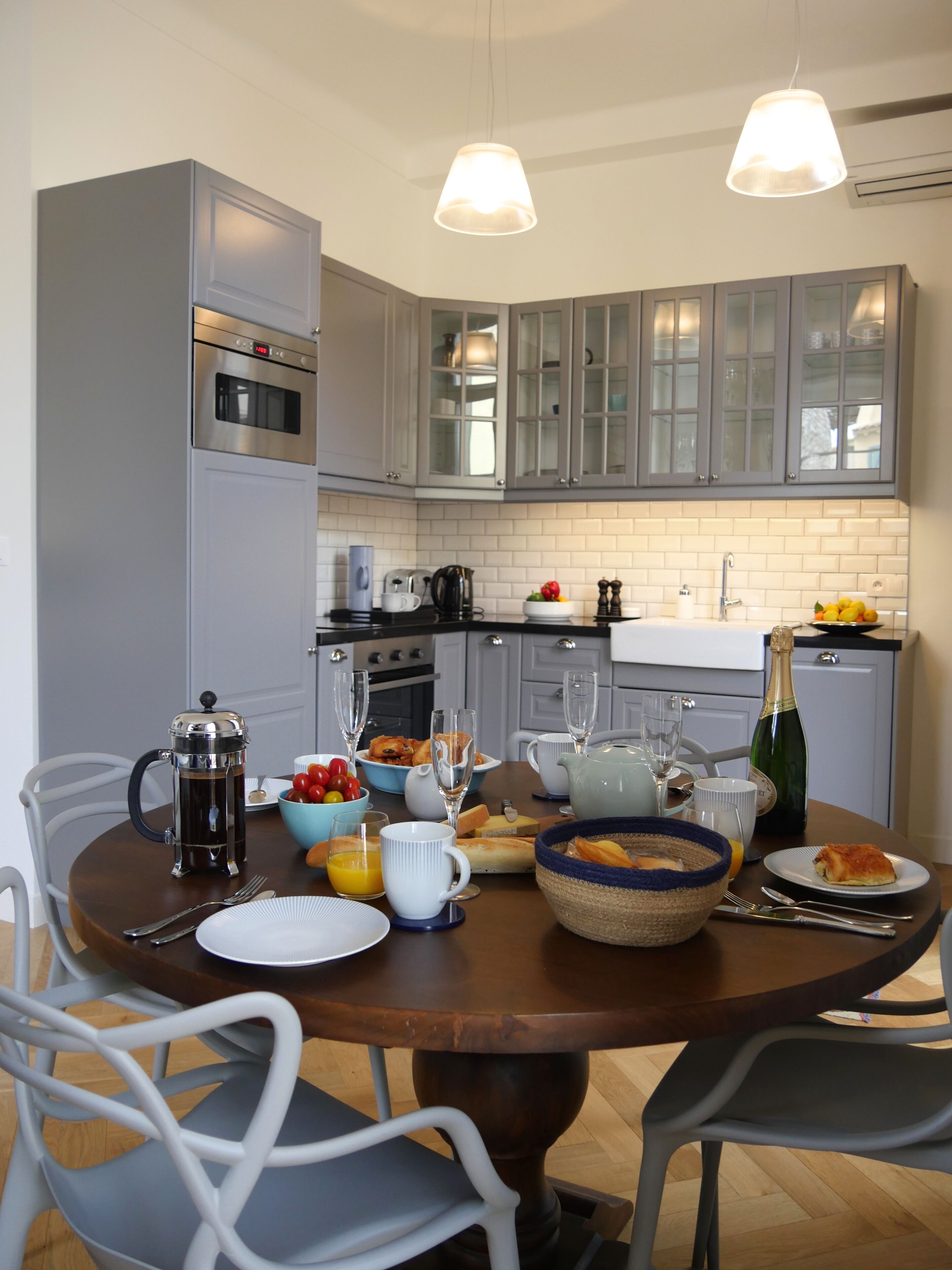 Une cuisine moderne avec des meubles gris, un four en acier inoxydable et une table à manger dressée pour le petit-déjeuner.