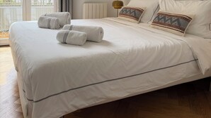 A neatly made bed with rolled towels, a radiator, and framed artwork on the wall.