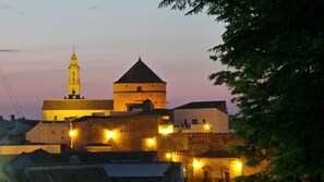 Un complesso di edifici storici con una torre imponente e una grande cupola, circondato da strutture più piccole ed illuminato da lampioni.