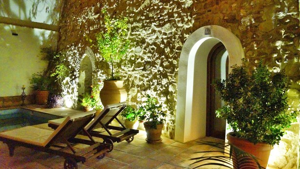 A stone-walled courtyard with a pool, lounge chairs, and potted plants.