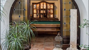 An arched doorway leading to a room with a wooden cabinet filled with books, a birdcage, and a small table with a candle.