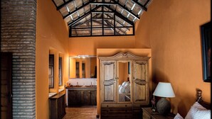 A room with a wooden cabinet, a bed, a nightstand with a lamp, and a large mirror.