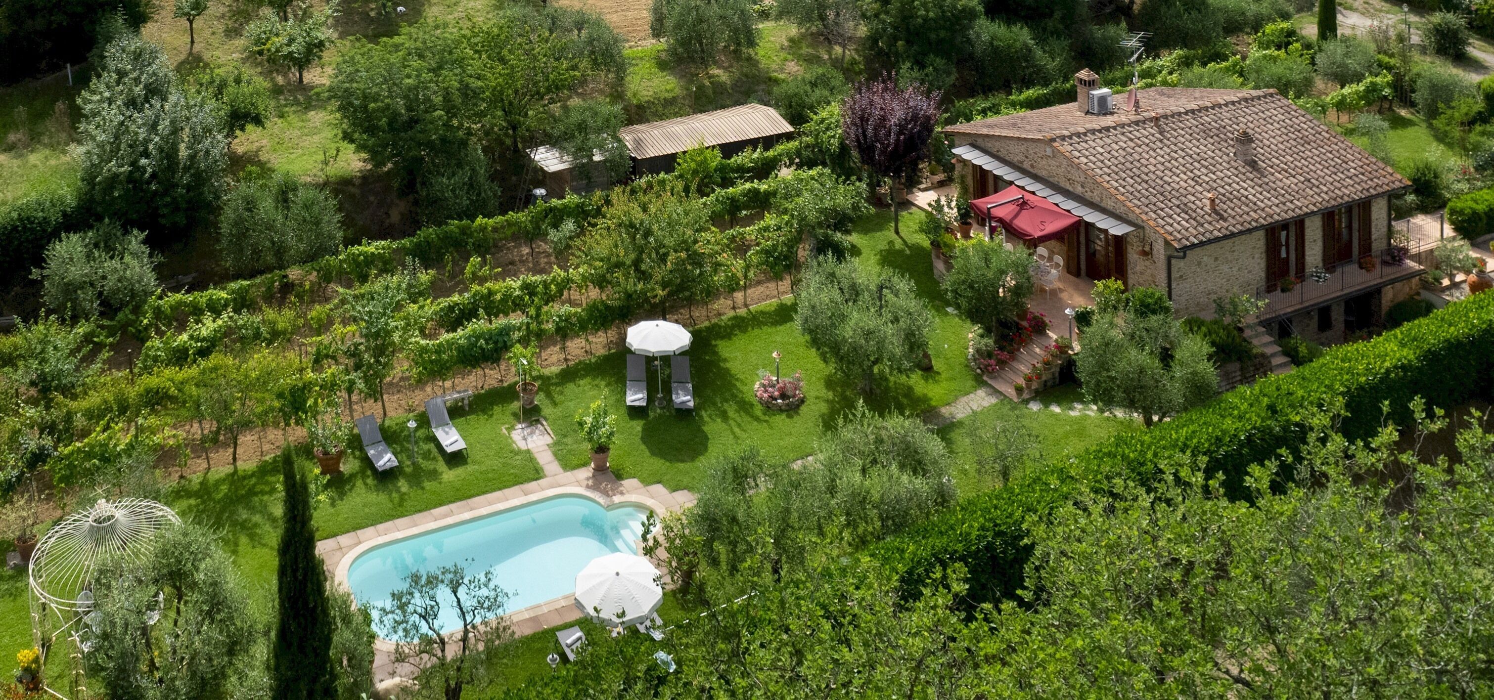 Vista aérea de uma propriedade com piscina, jardim e uma casa com telhado cerâmico.